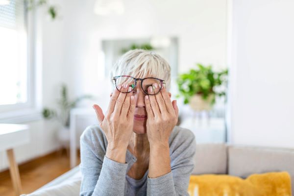 Mulher de meia idade esfregando os olhos - um dos sintomas do olho seco.