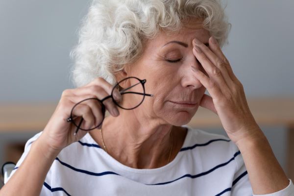 Na 3ª idade, entre os sintomas do glaucoma estão visão embaçada e dor de cabeça. Na imagem, uma senhora segura os óculos em uma mão enquanto a outra está sobre os olhos.
