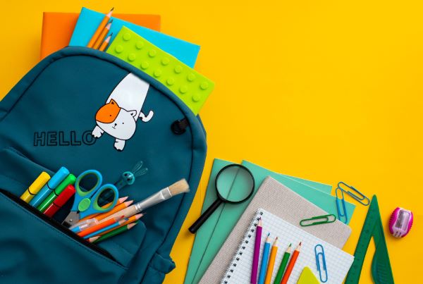 Mochila e materiais escolares coloridos deitados sobre um fundo amarelo.