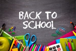 Quadro negro no qual está escrito Volta às aulas. Ao redor muitos materiais escolares.