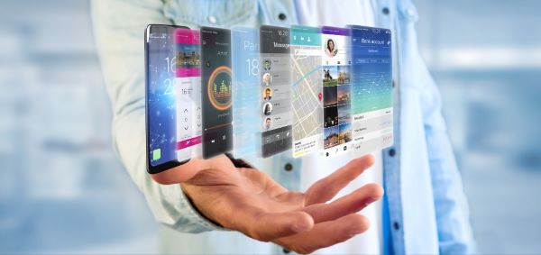 Homem com uma mão aberta, da qual surgem imagens de diversos smartphones.
Conceito do uso excessivo de telas digitais.