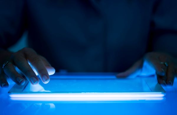 Homem usando um tablet de cuja tela emerge luz azul, que é extremamente prejudicial à visão.