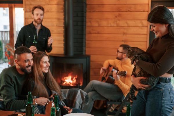 Grupo de amigos confraterniza dentro de casa junto à lareira onde o fogo trepida. Todos vestem roupas quentes para fugir do frio do inverno.