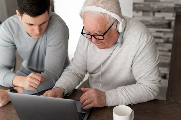 Idoso, junto a um pesquisador, realizando teste em um notebook para detectar Alzheimer.