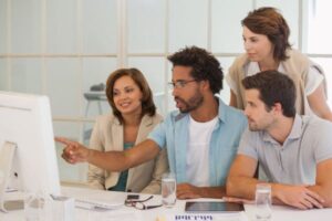 2 mulheres e 2 homens, em ambiente laboral, olham para a tela do computador e conversam sobre negócios.