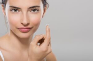 Mulher jovem segurando uma lente de contato no dedo indicador.