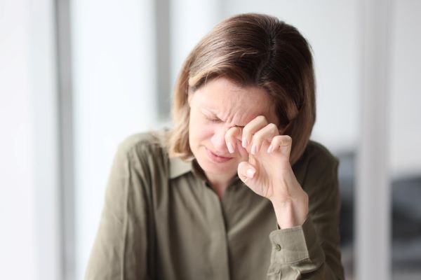 Mulher de meia idade, com cabelos castanhos, coça os olhos em sinal de desconforto ocular.
Durante a menopausa, é comum que ocorra a Síndrome do Olho Seco.