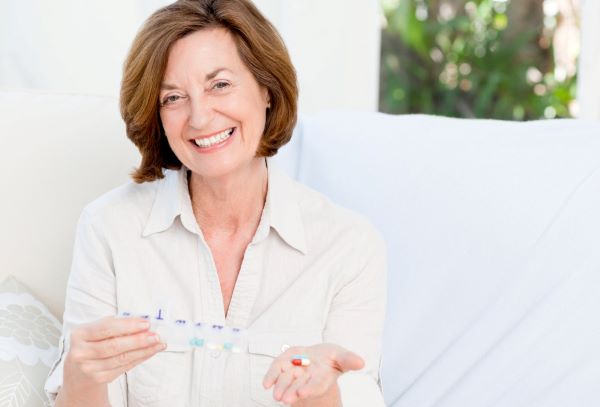Linda mulher madura sorri segurando nas mãos pílulas de reposição hormonal.