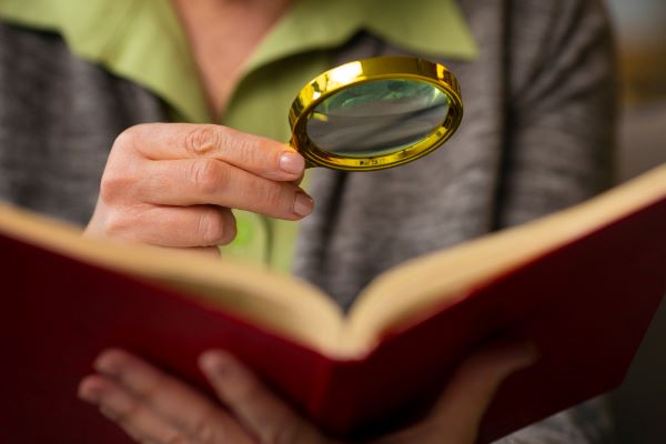 Mulher utilizando uma lupa para fazer leitura de livro.