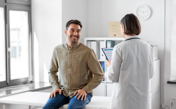 Homem sorridente, em consulta, com uma médica que avalia sua saúde geral.