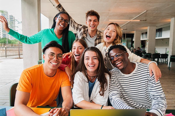 Grupo diverso de jovens, felizes, na biblioteca da escola.