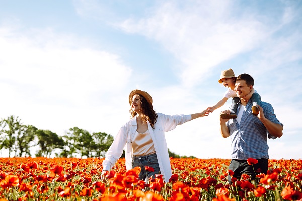 Família, casal e uma criança, passeia por uma plantação de flores vermelhas em um dia ensolarado.