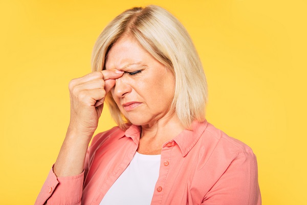 Mulher madura loira, com cabelos médios e lisos, aperta os olhos com os dedos indicador e polegar, indicando desconforto ocular.