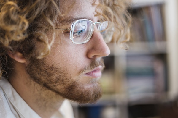 Jovem usando um par de óculos de grau para miopia. Ele tem cabelos encaracolados e loiros, e usa barba.