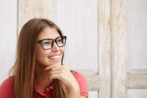 Linda jovem usnado blusa vermelha e óculos de grau com armação escura sorri.