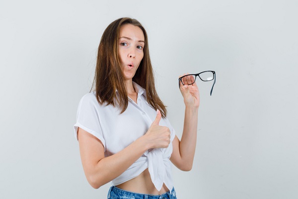 Paciente, feliz após ter realizado a cirurgia refrativa PRK , segura na mão esquerda seu par de óculos de grau que vai abandonar, enquanto com a direita faz sinal de positivo.