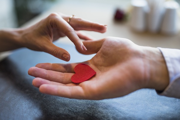 Gesto que simboliza a doação de órgãos, em especifico, a de córneas. Mão masculina oferece um coração vermelho para uma mão feminina.