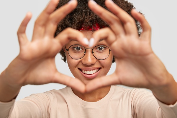 Linda jovem negra faz um coração com as mãos frente aos olhos.
