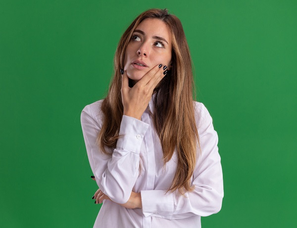Linda jovem com cabelos longos, vestindo uma camisa branca, demosntra expressão de dúvida sobre alguns vícios de refração.
