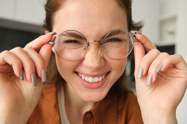 Close de linda jovem sorridente segurando os óculos de grau sobre os olhos.