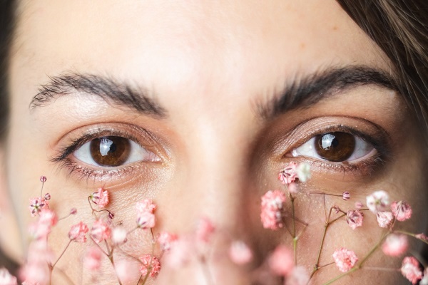 Close no rosto de uma mulher jovem bonita, com destaque para a beleza do olhar emoldurado por mini flores rosas.